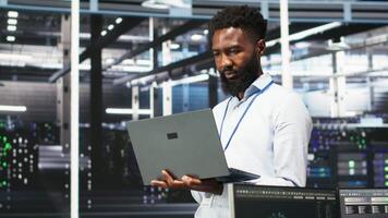 Vertical Data center programmer uses node tree software to identify equipment performance issues. African american server farm worker reviews data analysis graph to minimize hardware failures, camera B video