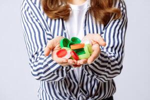 A woman is actively engaging in recycling by holding a collection of colorful plastic bottle caps in her hands. Her eco-friendly approach reflects awareness for environmental sustainability. photo