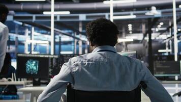 Vertical Server room programmer with paraplegia interprets data analytics graphs. Man in wheelchair using artificial intelligence program showing predictive system metrics in data center, camera A video