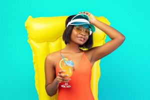 Carefree black lady in bikini lying on inflatable lilo with glass of tropical cocktail over blue background, panorama. Charming African American woman sunbathing on pool float during summer vacation photo