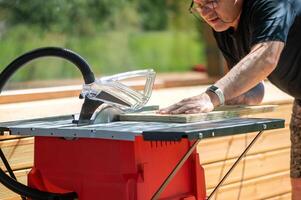 A male carpenter saws chipboard and a wooden board with a circular saw on the machine. Furniture production. photo