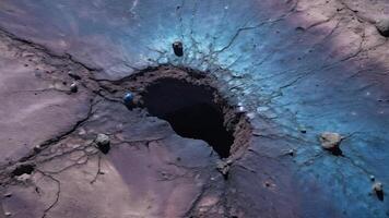 an aerial view of a large crack in the ground revealing a deep hole, with purple and blue textures on the surface photo