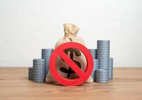 The NO prohibition sign covers the dollar money bag and stacks of coins. Freezing or confiscation of financial assets. Anti-money laundering actions, asset seizure, or economic retaliation. photo