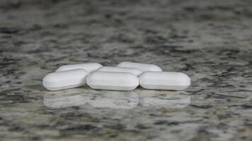 Six white pills are scattered on a light colored stone countertop photo