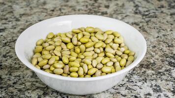 Bowl filled with dried Canary beans on a granite countertop showcasing their natural colors and textures photo