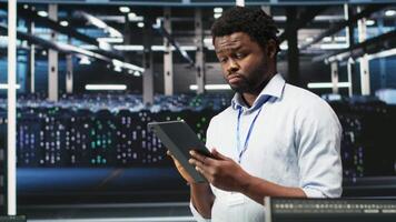 Data center engineer using tablet to interpret data analytics graphs. Server room worker using artificial intelligence displaying system performance predictive metrics, camera B video
