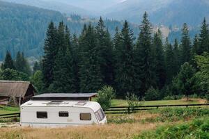 Scenic caravan parked in a tranquil meadow surrounded by tall trees and Carpathians mountains photo