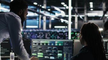 Data center manager supervising engineer using node tree tool to identify equipment performance issues. Server hub team leader talks with IT specialist reviewing data analysis graph, camera B video