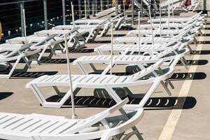 Lounge chairs arranged in a row on a sunny deck by the water during daytime photo