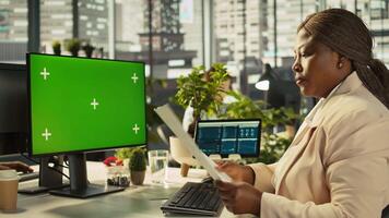 Employee at work using isolated screen PC display to finish project tasks. African american office clerk in workplace reading data statistics on mockup computer monitor, camera B video