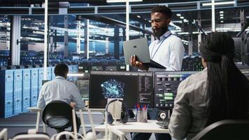 Happy data center admin uses node tree programming on laptop, doing high five with coworker. Smiling server farm worker greeting colleague, reviewing data analysis graph, camera A video