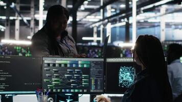 Vertical Data center manager supervising technician using node tree software to analyze datasets. Server room team leader oversees IT expert using visual programming tools to improve gear performance, camera B video