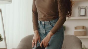 A young Middle Eastern woman is relaxing at home, dressed casually in a long-sleeve top and jeans. She appears engaged and comfortable in her modern living environment, surrounded by personal touches. video