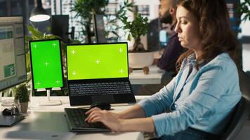 Office clerk uses chroma key devices to read data statistics on display after audit. Employee at work using green screen laptop and tablet to check progress done on commissioned project, camera A video
