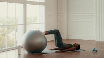 An African American woman engages in a workout session at home, using a stability ball for core strength training. The bright indoor space is designed for a healthy lifestyle. video