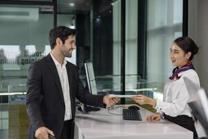 Caucasian businessman passenger is receiving boarding pass from the airline ground crew at check in counter at departure terminal into the airplane for final inspection before boarding the plane photo