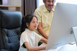 Young asian schoolgirl is doing class homework assignment at home with grandfather advice for education and study photo