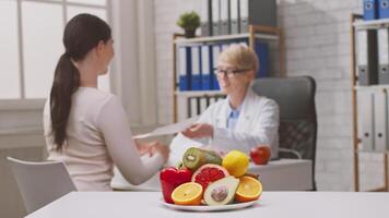 A dietitian discusses nutrition plans with a client in a modern clinic. Fresh fruits are displayed on the table, enhancing the focus on healthy eating habits and dietary advice. video