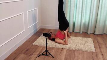 middle-aged woman doing yoga on a floor at home and also broadcasting to her followers using a smartphone mounted on a tripod video