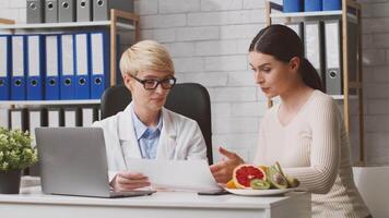 A dietitian in a clinic discusses a personalized nutrition plan with a woman patient. Fresh fruits are present on the table, emphasizing healthy food choices and dietary guidance. video