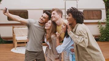 A group of diverse friends takes a selfie outdoors while relaxing at their summer camping spot. They share laughter and joy, embracing their connection in nature. video