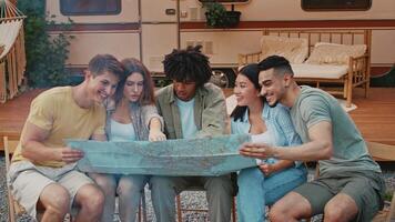 A group of diverse friends is gathered around a large map, excitedly discussing their camping plans. They are enjoying their summer weekend outdoors, surrounded by nature. video