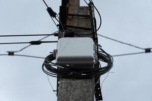 Communication equipment attached to a utility pole, surrounded by tangled wires, set against a backdrop of a grey overcast sky with minimal visibility photo