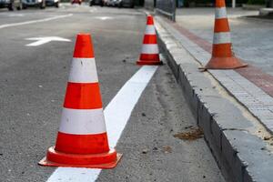 Traffic cones line the street, indicating ongoing construction work. Vehicles are rerouted while new boundaries are being established in an urban neighborhood photo