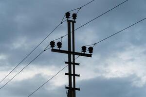 A power pole stands tall with electrical lines stretching across a darkening sky. Clouds gather around, creating a moody atmosphere during early evening photo