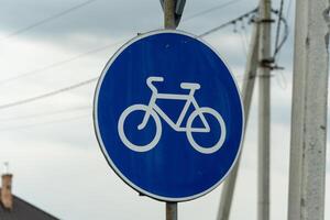 A blue circular sign displays a white bicycle icon, marking a designated lane for cyclists in an urban setting under overcast skies photo