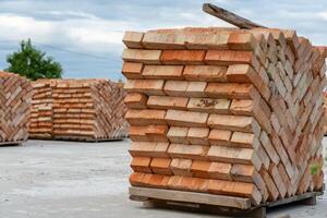 Several neatly arranged stacks of bricks are visible at a construction yard, showcasing their earthy tones against a backdrop of overcast skies photo