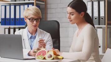 A dietitian discusses dietary habits with a client in a clinic. The dietitian highlights healthy food options like avocados while providing expert advice on nutrition and meal planning. video