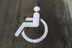 A white accessibility symbol is painted on a gray concrete surface, designating a parking space for individuals with disabilities in an urban setting photo