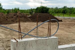 Workers are laying the foundation at a construction site, where rebar and electrical conduit are visible against a backdrop of earth mounds and cloudy skies photo