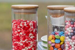 Clear jars display an assortment of heart-shaped candies and vibrant round sweets at an outdoor setting. The atmosphere is cheerful and festive photo