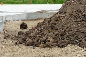 Pile of soil and stones at a construction site, with scattered debris and an unfinished concrete slab visible in the background on a cloudy day photo
