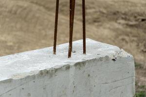 Exposed rebar protrudes from a concrete block, indicating ongoing construction work in a rural area under clear skies during the afternoon photo