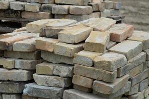 Piles of weathered bricks are arranged neatly at a construction site, waiting to be used in various building projects under clear daylight photo