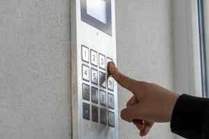A hand is pressing the number three on a sleek keypad mounted on a wall, likely to gain access to the building, with soft natural light illuminating the area photo