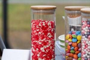 Clear jars filled with vibrant heart-shaped candies and colorful chocolate-coated sweets attract attention at an outdoor celebration in the afternoon light photo