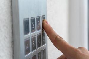 A person is using their finger to press the number three on a metallic keypad located beside a door. Bright light fills the area, indicating daytime photo