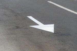 A clear white arrow is marked on the asphalt surface, guiding vehicles to turn left at a busy urban intersection under bright daylight photo