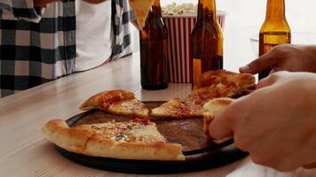 A diverse group of millennials enjoys a lively home gathering, sharing pizza and drinks while laughing and having fun together in a cozy setting. video