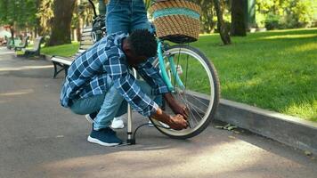 In a vibrant park setting, a young couple is having fun while adjusting a bicycle tire. video