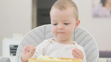 Toddler eating mashed potatoes with spoon in high chair video