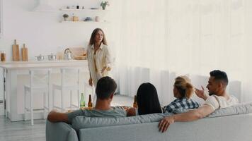 A group of diverse millennials is having a fun time together at home. They are seated on a couch while one friend animatedly shares a story, creating a relaxed and joyful atmosphere. video