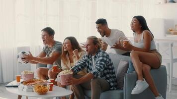 A group of diverse friends gathers in a cozy living room to watch a game. They cheer excitedly, holding snacks and drinks, creating a fun and lively atmosphere together. video