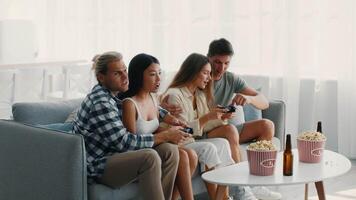 Four friends gather in a cozy living room, having a fun gaming night. They play games together on a comfortable couch, surrounded by snacks and drinks, celebrating friendship and leisure. video