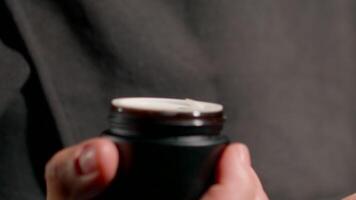 woman wearing hijab is engaged in her skincare routine home. She carefully holds small jar focusing on its contents as she prepares for relaxing evening video