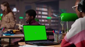 Young student uses mockup display while doing research for exam preparations, reading educational information from reliable academic sources. Pupil completes her notes in the textbook. Camera A. video